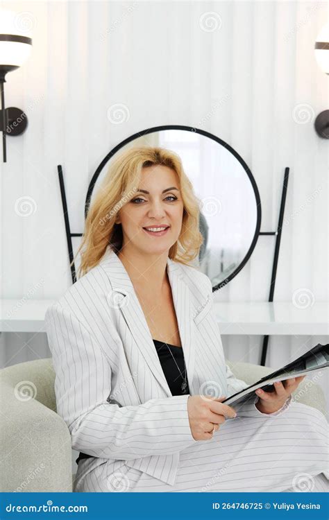 A Beautiful Slender Mature Woman Entrepreneur In White Trousers And A Jacket Sits In A Chair