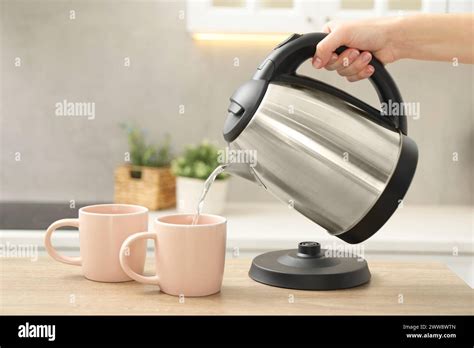 Woman Pouring Hot Water From Electric Kettle Into Cup In Kitchen