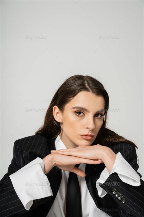 Portrait Of Brunette Woman In Stylish Attire Posing With Hands Under Chin While Looking At
