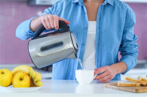 Mulher derramando água fervida em um copo de uma chaleira elétrica para