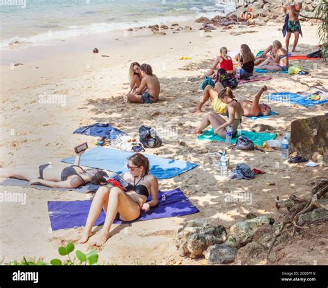 Western Tourists Wearing Bikinis Sunbathing And Relaxing On White Sand