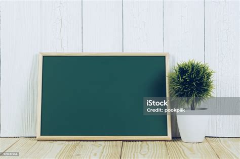 Blank Green Chalkborad With Wood Frame And Little Decorative Tree In White Vase On Wooden Table