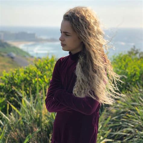 A Woman With Long Blonde Hair Standing On Top Of A Hill Next To The Ocean