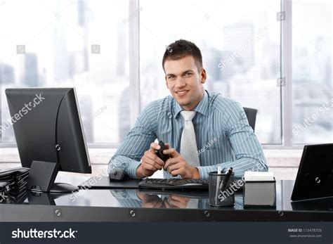 Young Manager Sitting At Desk In Bright Office Smiling Confidently