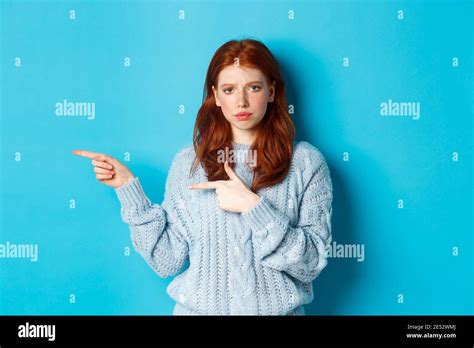 Skeptical And Displeased Redhead Girl Pointing Fingers Left With Upset Face Standing