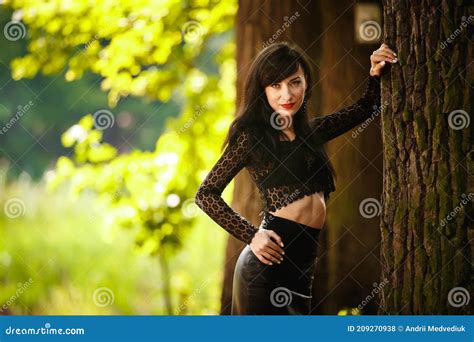 Brunette Girl In A Lace Blouse And Leather Skirt With High Heels Posing Near A Tree In The Woods