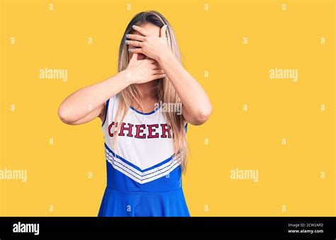 Young Beautiful Blonde Woman Wearing Cheerleader Uniform Covering Eyes