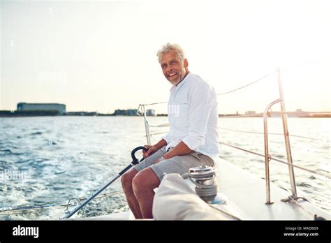 Smiling Mature Man Sitting On The Deck Of His Boat Enjoying A Sunny Day Sailing On The Open