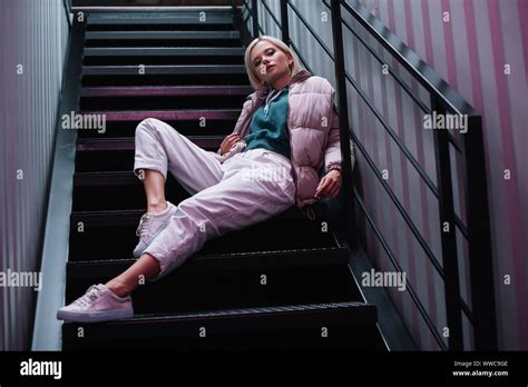 Confident Blonde Girl In Down Jacket And Sneakers Sitting On Stairs Stock Photo Alamy