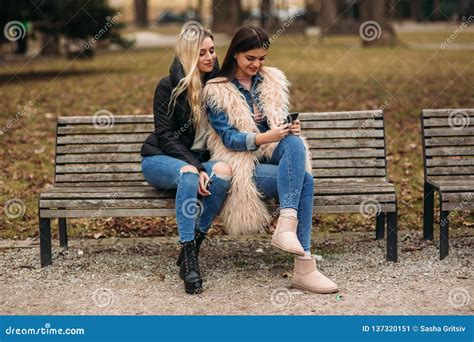 Two Girls Sitting On The Bench Outdoors Autumn Weather Stock Image