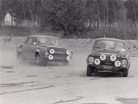 two cars driving on a dirt road with trees in the background