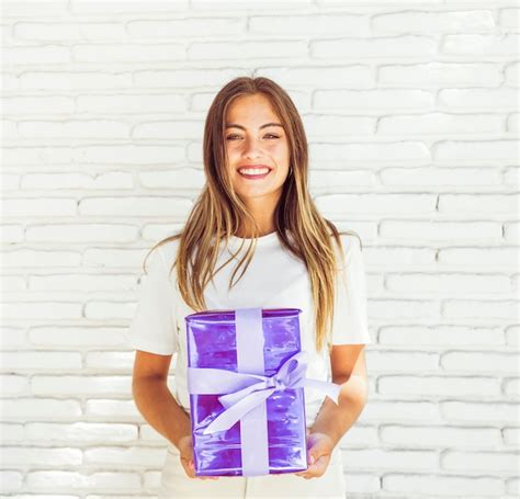 Mujer Feliz Que Sostiene La Caja De Regalo Contra La Pared De Ladrillo