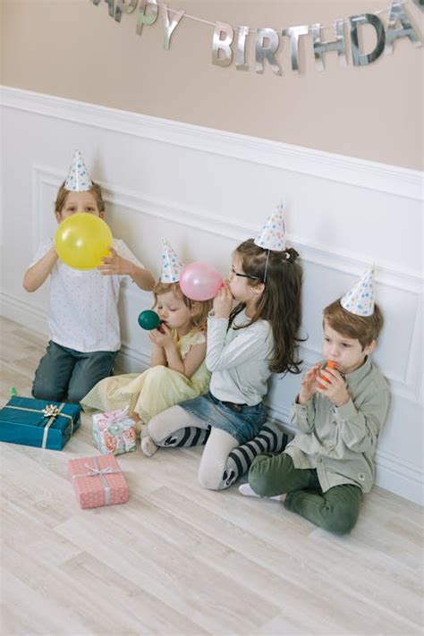 A Group of Children with Party Hats Sitting on the Floor Blowing ...