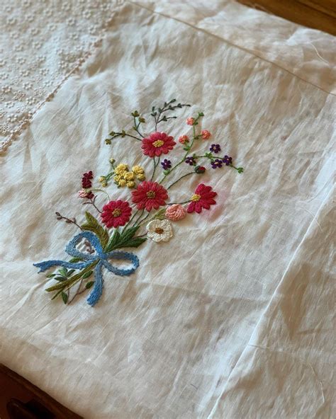 An Embroidered Piece Of Cloth With Flowers On It Sitting On A Wooden