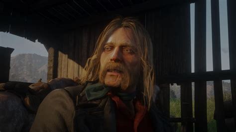 a man with long hair and beard standing in front of a wooden structure looking at the camera