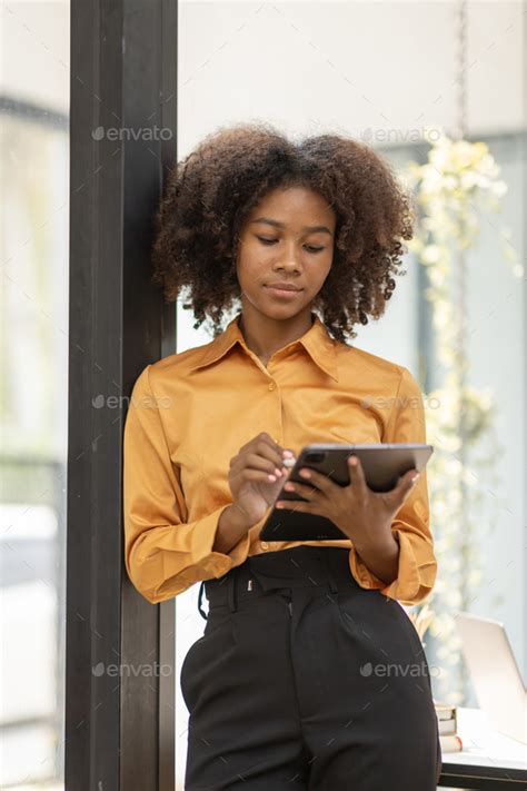 Beautiful Authentic Latina Female With Afro Hair Sitting At A Desk In A Cozy Living Room And