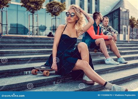 Sexy Blonde Frau Im Schwarzen Kleid Sitzt Auf Einem Longboard Stockfoto