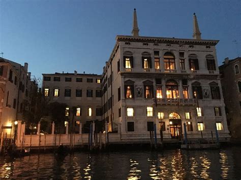 An Old Building Is Lit Up At Night On The Water S Edge In Front Of Some