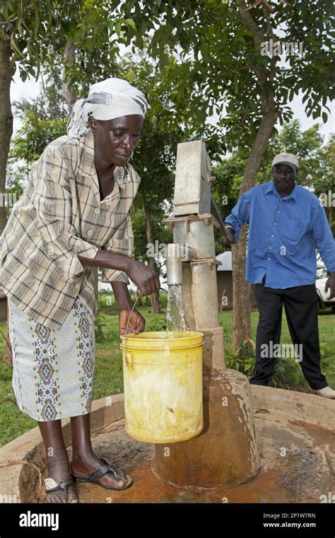 Woman Filling Buckets With Clear Water At The Well Of A Hand Pump In