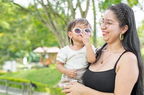 Premium Photo Latina Mother Holding Her Smiling Baby Daughter While The Baby Puts On Her Glasses