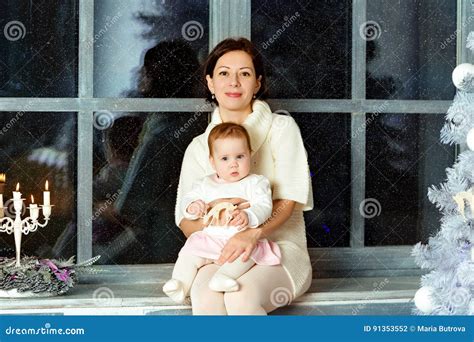 Mutter Brunette Der Auf Fenster Und Umarmungen Der Kleine Nette Mollige G Sitzt Stockfoto