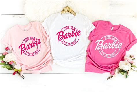 Three T Shirts With The Word Barbie On Them Are Sitting Next To Some