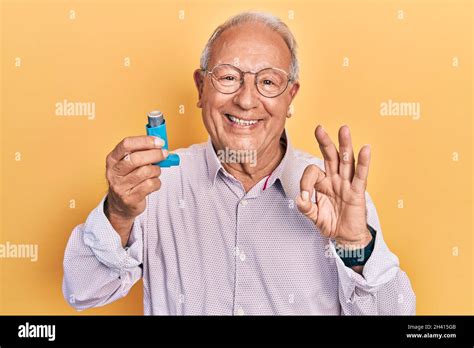 Senior Man With Grey Hair Holding Medical Asthma Inhaler Doing Ok Sign