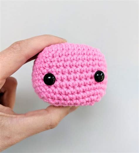 A Pink Crocheted Object With Black Eyes Is Held In Someones Hand