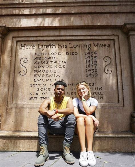 A Man And Woman Sitting On A Bench In Front Of A Wall That Has Writing