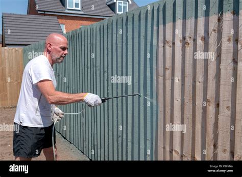 Man using a paint sprayer to paint a garden fence green Stock Photo - Alamy