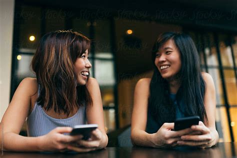 Asian Friends Women Using The Mobile In The Coffee Shop By Stocksy