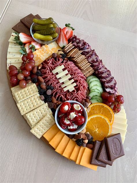 A Platter Filled With Cheese Crackers Fruit And Meats On A White Table