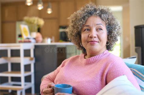 Mature Woman Sitting On Sofa At Home Relaxing With Hot Drink Stock