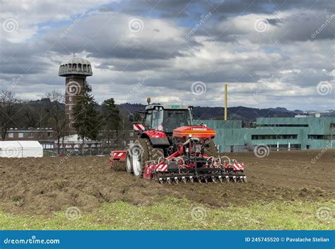 Tractor Plows The Field In Front Of Some Agricultural Buildings On A