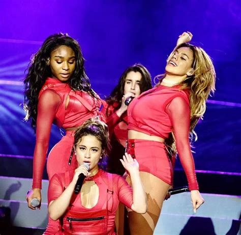 Three Women In Red Outfits On Stage With One Holding A Microphone And