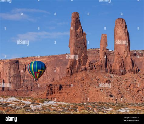 A Hot Air Balloon Flying By The Three Sisters In The Monument Valley