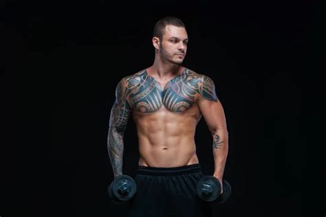 The Man With A Muscular Naked Torso With Tattoos On The Dark Background ABS Stock Photo