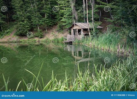 Wooden House On The Shore Of A Small Lake Surrounded By Trees And