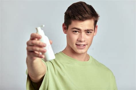 Young Handsome Smiling Brown Haired Guy Holding A Bottle Of Facial Wash