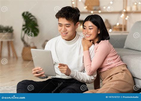 Happy Korean Couple Using Tablet Computer Sitting At Home Stock Image