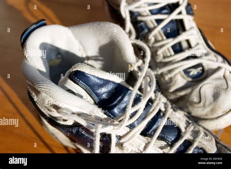 A Pair Of White Tennis Shoes With Undone Shoe Laces Sit Next To Each