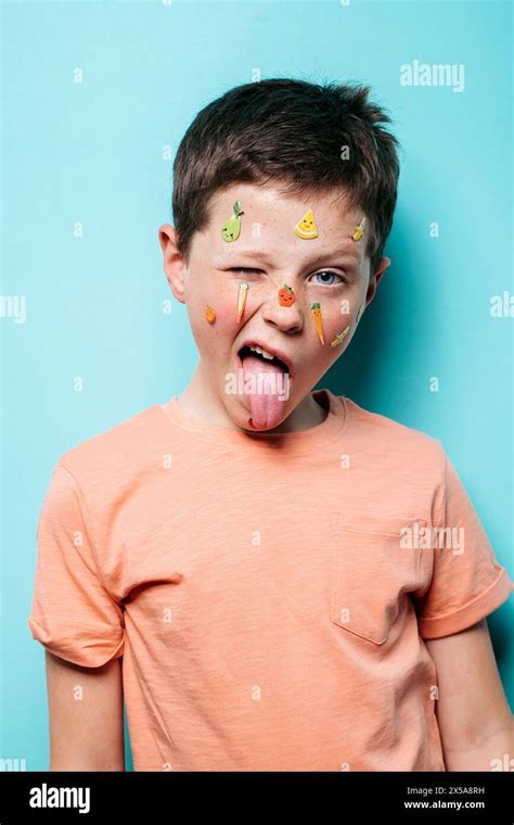 A Young Boy With Quirky Fruit Themed Stickers Playfully Adorning His Face Sticks Out His Tongue