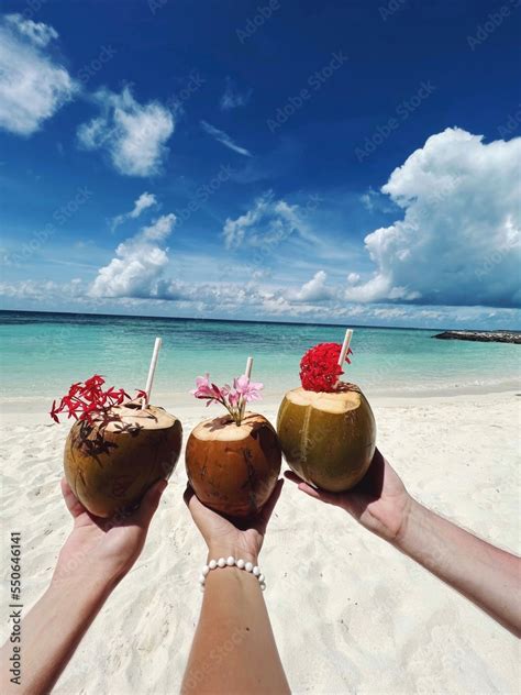 Tropical coconut cocktails in the hands of three people on the beach of ...