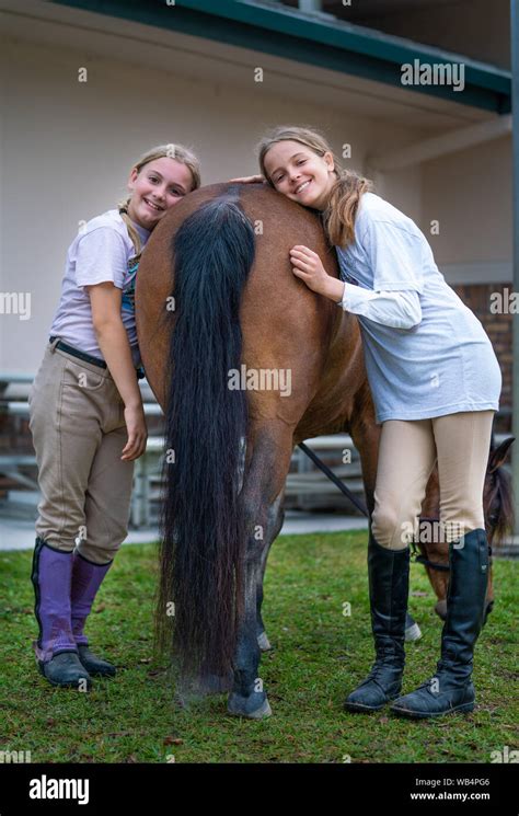 Two equestrian girls are standing next to the horse's back and smiling ...