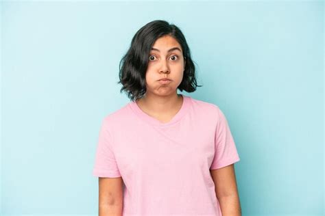 Joven latina aislada sobre fondo azul sopla mejillas tiene expresión cansada concepto de