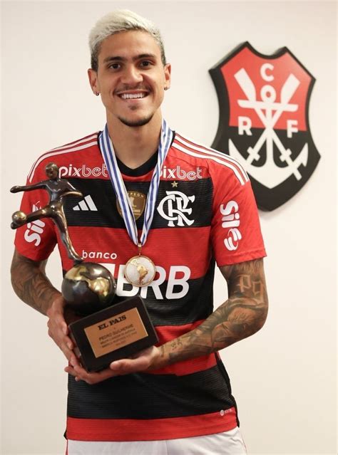 A Man Holding An Award In Front Of Two Other Awards On The Wall Behind Him