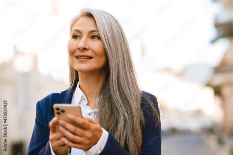 Mature Asian Woman With Grey Hair Smiling And Using Mobile Phone Stock Photo Adobe Stock