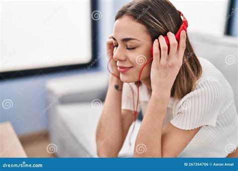 Young Beautiful Hispanic Woman Listening To Music Sitting On Sofa At