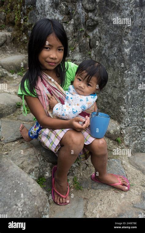 Young Filipino girl holding her little sister on her lap while feeding ...