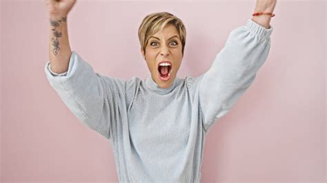 Excited Woman With Short Blonde Hair Celebrating Against A Pink Wall Portraying Youthful Energy
